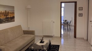 A living room with a sofa, a coffee table, a lamp, a radiator, and a dining area in the background. - ANNA LITTLE HOUSE Vacation Home (Bari)