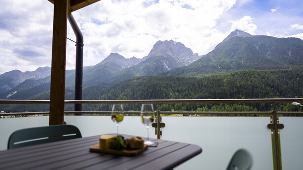 Ein Tisch mit Mahlzeit und Weingläsern, mit Blick auf einen See und Berge.