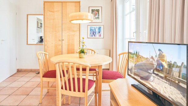 A dining area with a wooden table and chairs, a television, and a window with curtains. - Moderne Ferienwohnung im Seepark Sellin mit Balkon (Sellin)