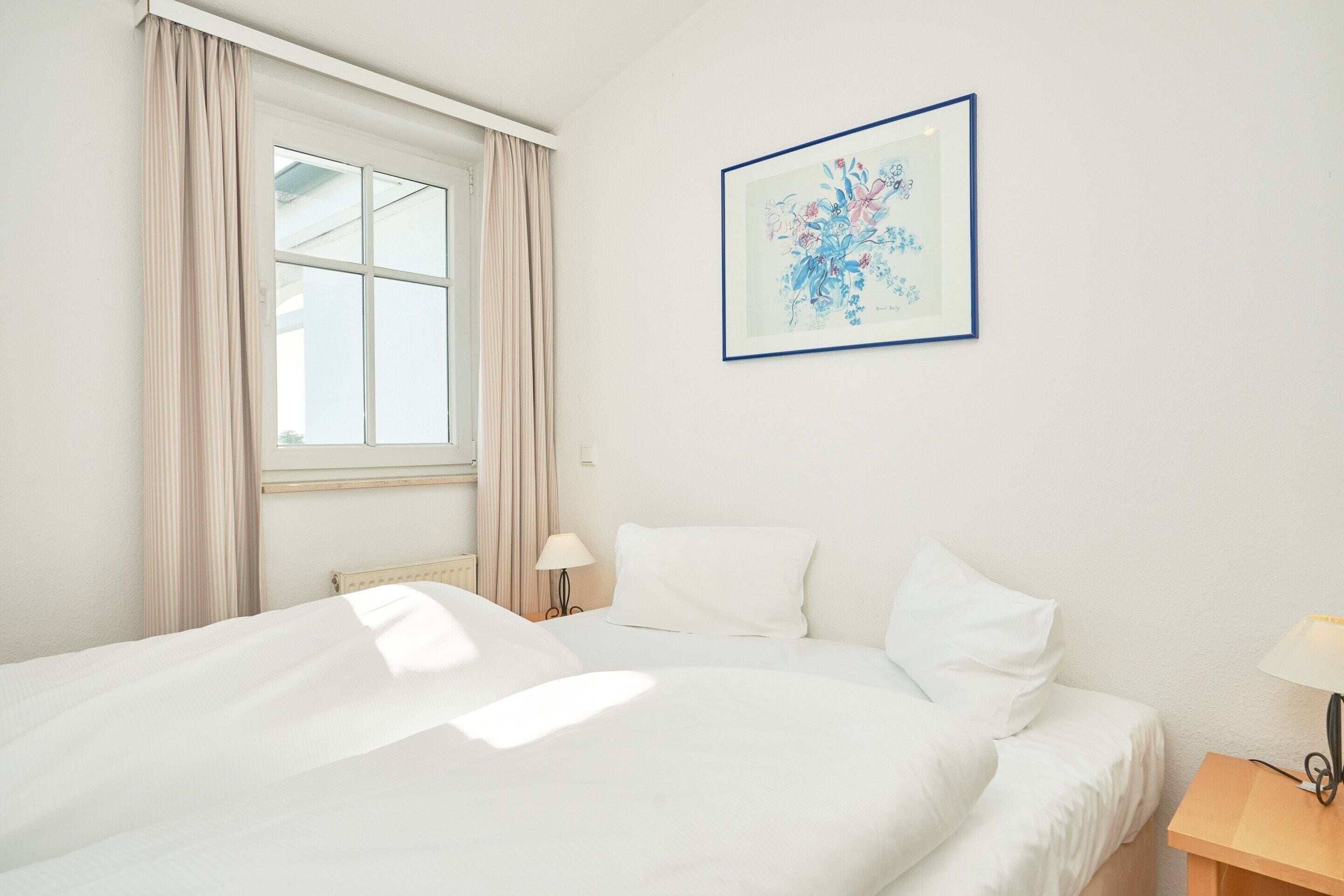 A hotel room with a bed, a nightstand, a lamp, a window with curtains, and a framed picture on the wall.