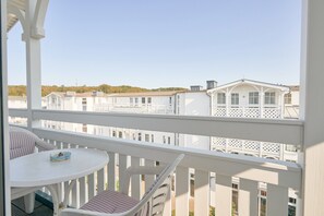 Un balcon avec une balustrade blanche, une table ronde et une chaise dotée de coussins à rayures.