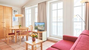 A modern living room with a red sofa, wooden dining table, chairs, a TV, and large windows. - Moderne Ferienwohnung im Seepark Sellin mit Balkon (Sellin)