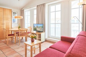 A modern living room with a red sofa, wooden dining table, chairs, a TV, and large windows. - Moderne Ferienwohnung im Seepark Sellin mit Balkon (Sellin)