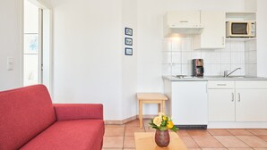 A modern kitchen with white cabinets, a microwave, and a coffee maker. There is a red sofa and a small wooden stool. - Moderne Ferienwohnung im Seepark Sellin mit Balkon (Sellin)