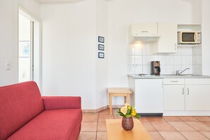 A modern kitchen with white cabinets, a microwave, and a coffee maker. There is a red sofa and a small wooden stool. - Moderne Ferienwohnung im Seepark Sellin mit Balkon (Sellin)