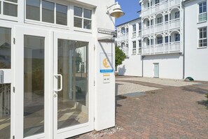 A white building with a glass door entrance, a sign indicating 'Seeparkpromenade,' and a blue sign with a yellow symbol. - Moderne Ferienwohnung im Seepark Sellin mit Balkon (Sellin)
