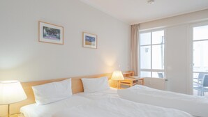 Quarto de hotel com duas camas, uma escrivaninha, uma cadeira e uma janela.