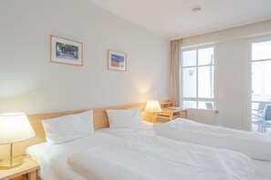 A hotel room with two beds, a desk, a chair, and a window. - Ostseeurlaub Ferienwohnung mit Balkon in Sellin (Sellin)