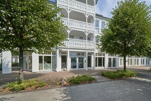 A modern building with a white facade, multiple balconies, and a paved entrance area with greenery. - Ostseeurlaub Ferienwohnung mit Balkon in Sellin (Sellin)