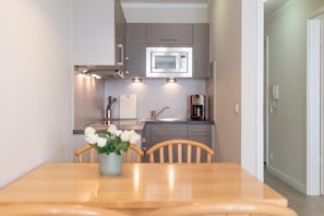 A compact kitchen with a microwave, coffee maker, and a dining table with chairs. - Ostseeurlaub Ferienwohnung mit Balkon in Sellin (Sellin)