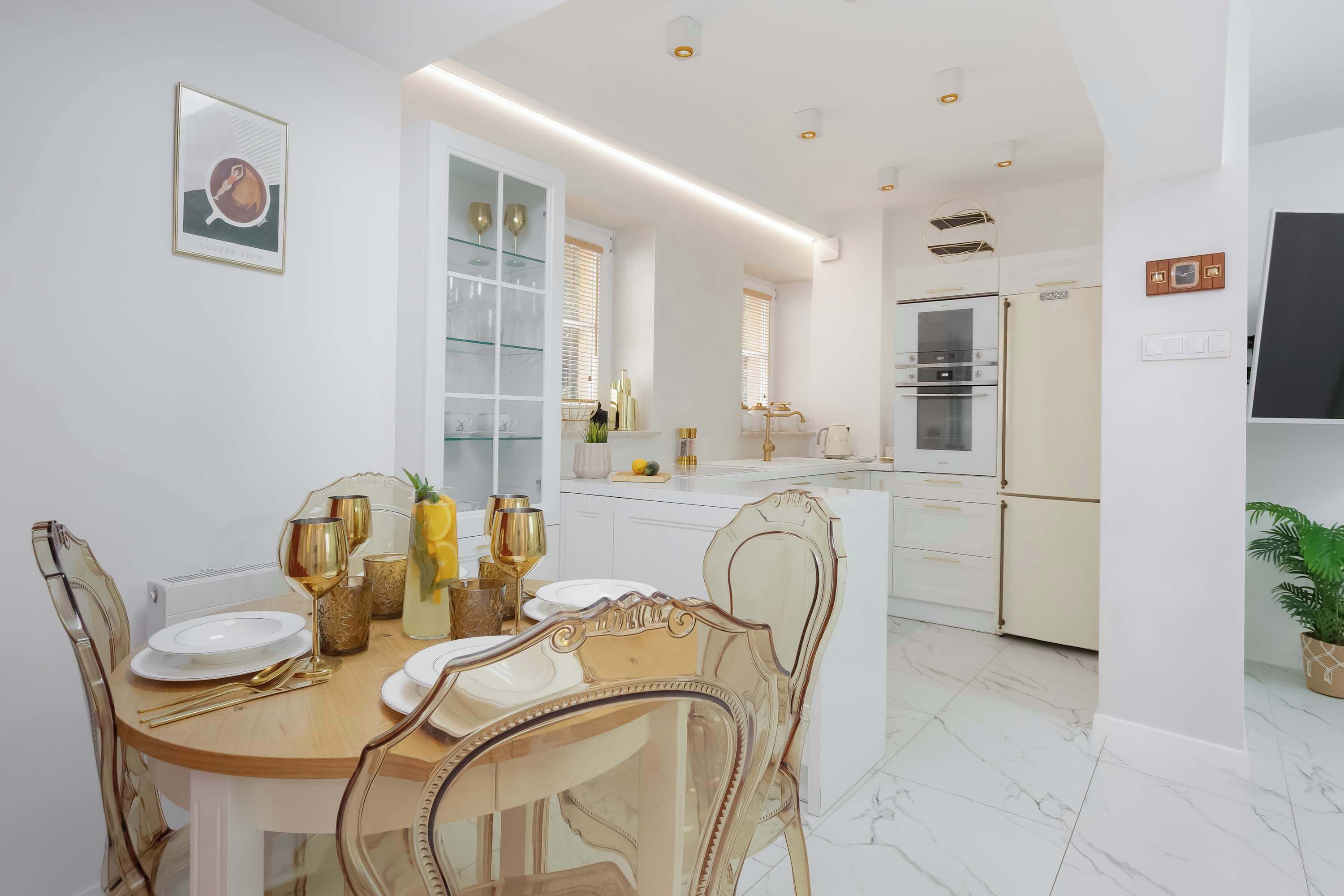 Une cuisine moderne avec des meubles blancs, un four encastré et un coin repas comprenant une table et des chaises en bois.