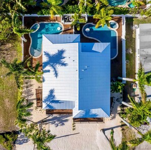 Ein Luftbild eines Resorts mit einem großen rechteckigen Pool, kleineren kreisförmigen Pools und umliegenden Palmen.