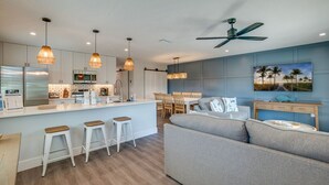 Une cuisine moderne avec des luminaires suspendus, un coin repas avec une table et des chaises, un canapé et un ventilateur de plafond.