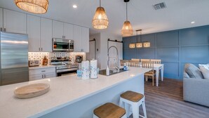 Une cuisine moderne avec des meubles blancs, des appareils en acier inoxydable et un îlot central doté de tabourets.