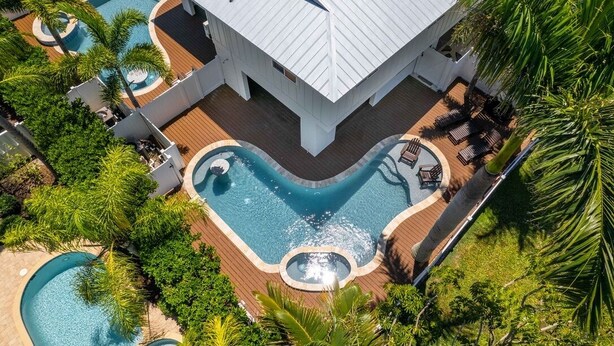 Une grande maison avec une piscine, entourée de palmiers et dotée d’une terrasse.