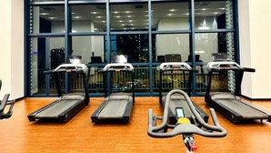 Ein Fitnessstudio mit Laufbändern und Trainingsgeräten, großen Fenstern mit Blick auf die Stadt und Holzboden.