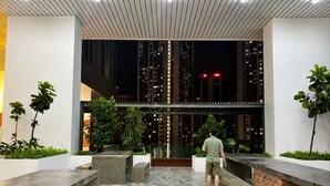Ein moderner Außenbereich mit einem Mann, einem Pool, Bänken und Blick auf hohe Gebäude bei Nacht.