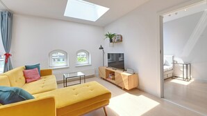 Sala de estar moderna com sofá, TV e claraboia.