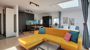 Uma sala de estar moderna com um sofá amarelo, uma mesa de centro de vidro e uma cozinha ao fundo.