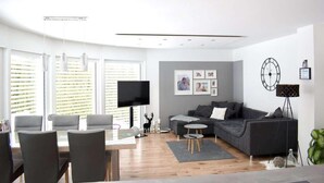 A modern living room with a grey sofa, a flat-screen TV, and a dining area with chairs and a table.