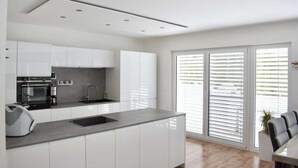A modern kitchen with white cabinets, a built-in oven, and a large window with blinds.