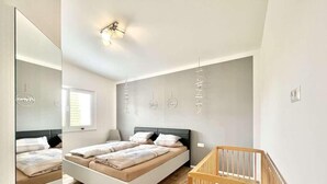 A modern bedroom with a large bed, a wooden crib, a mirror, and a wall-mounted light fixture.