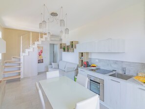 A modern kitchen with white cabinetry, a built-in oven, and a dining area with a white table and chairs. - La Casa di Giulia (Borghetto Santo Spirito)