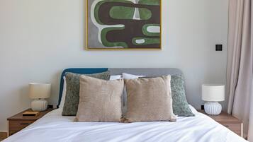 A neatly made bed with two pillows, a bedside table with a lamp, and a wall-mounted abstract painting.