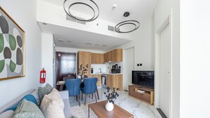 A modern living room with a sofa, coffee table, and TV. There is a dining area with chairs and a kitchen in the background. - Bloomfields 1BR Al Maryah Vista  (Abu Dhabi)