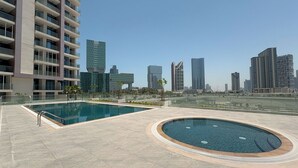A rooftop pool area with a large rectangular pool and a smaller circular hot tub, surrounded by a tiled deck. - Bloomfields 1BR Al Maryah Vista  (Abu Dhabi)