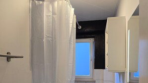 Un baño con cortina de ducha, inodoro, lavamanos con grifo y ventana.