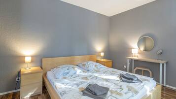 Ein Schlafzimmer mit einem Bett, Nachttischlampen, einem Schreibtisch mit Spiegel und einem Sessel.