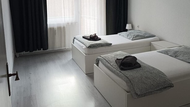 Habitación de hotel con dos camas, una ventana con cortinas, una lámpara y un radiador.