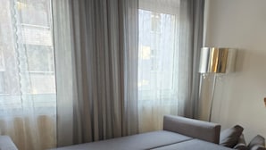 Una habitación con cama, sofá, lámpara y ventana con cortinas.