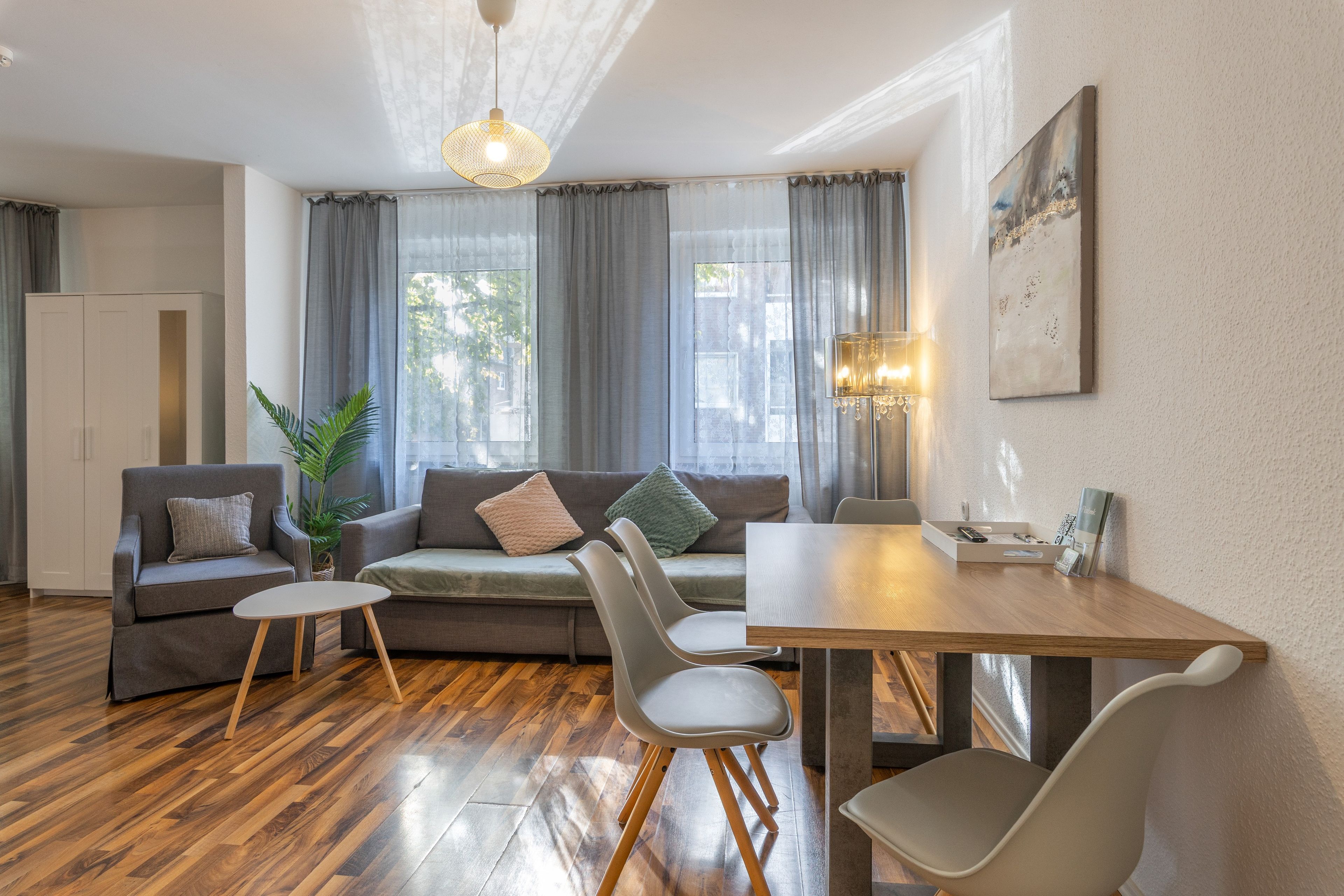 A modern living room with a sofa, chairs, a dining table, and a large window with curtains.
