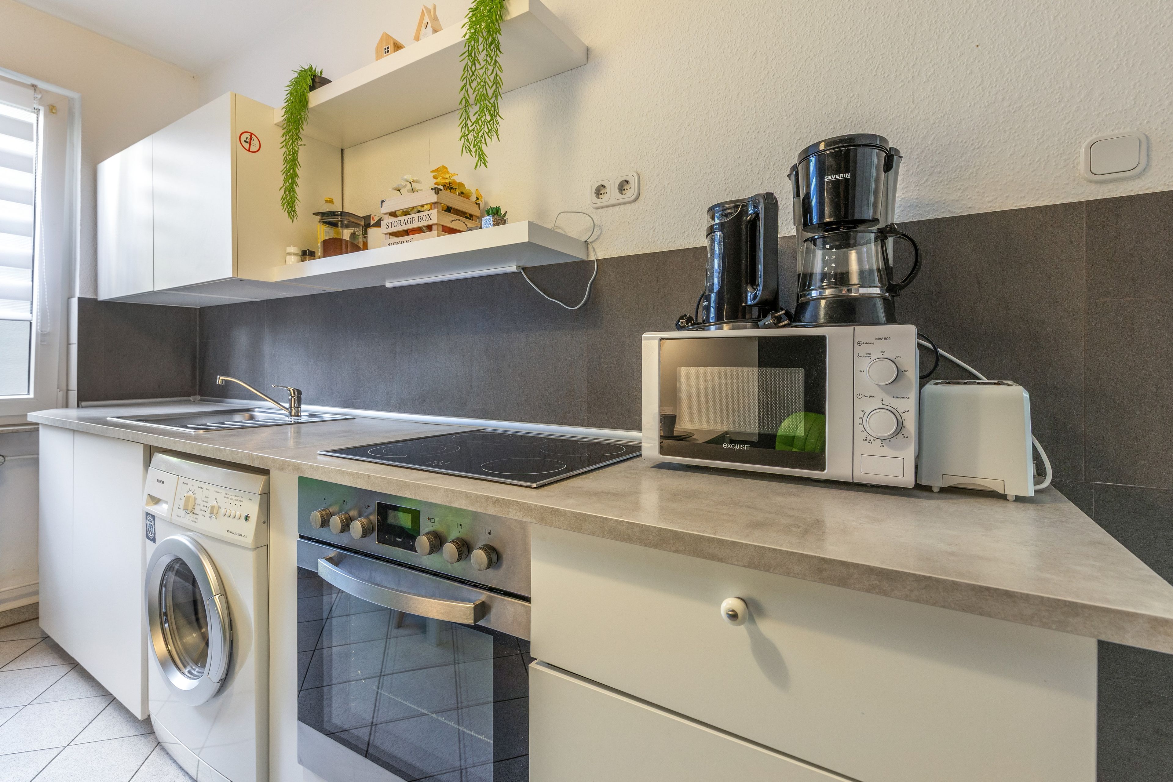 A modern kitchen with a built-in washing machine, a microwave, and a coffee maker.