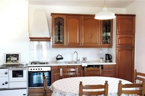 A kitchen with wooden cabinets, a stove, an oven, a sink, and a dining table with chairs. - Sunny home with a terrace offering an unobstructed view (Valbandon)