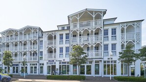 A multi-story hotel with a white exterior, multiple balconies, and a paved entrance area. - Ferienwohnung in Sellin mit Balkon und Wlan (Sellin)