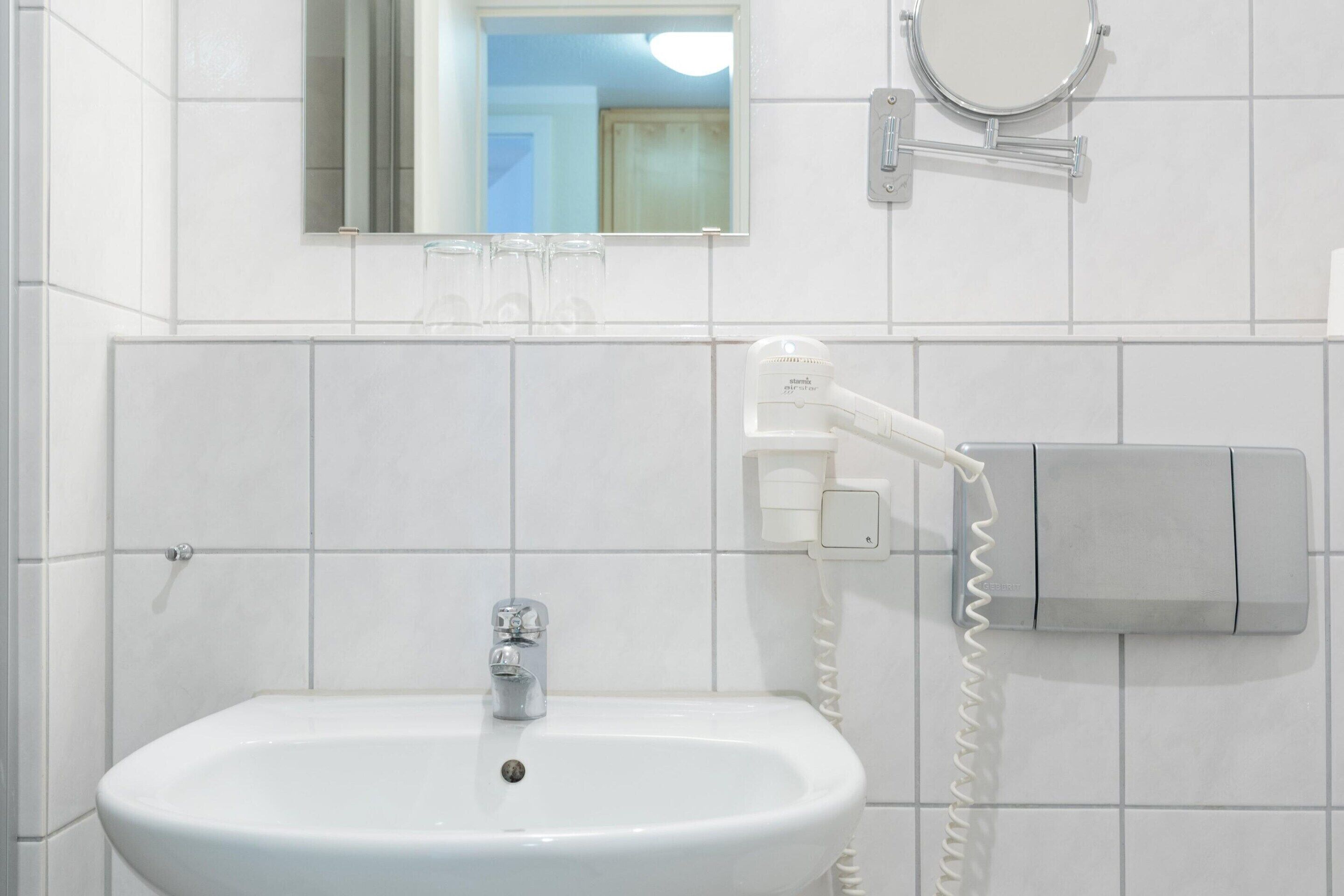 Een badkamer met een witte wastafel, een spiegel en een aan de muur bevestigde haardroger.
