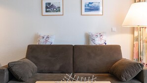 A brown sofa with two pillows, a metal fruit bowl on a wooden table, and two framed pictures on the wall. - Ferienwohnung in Sellin mit Balkon und Wlan (Sellin)