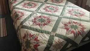 A bed with a quilt, a wooden headboard, a nightstand with a lamp, and a wall with wooden paneling.