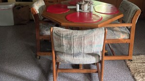 A dining area with a wooden table, four chairs, and a kitchen in the background.