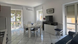 Um apartamento moderno com cozinha, sala de jantar e sala de estar. Possui uma varanda com vista, uma televisão e uma lareira.