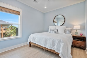 A bedroom with a large bed, a nightstand, a mirror, and a window with a view of a building and palm trees. - The Big Fish on Redfish - amazing views, hot tub, outdoor bar, and more!! (Crystal Beach)