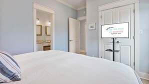 A bedroom with a bed, a mirror, a door, and a wall-mounted TV displaying text. - The Big Fish on Redfish - amazing views, hot tub, outdoor bar, and more!! (Crystal Beach)