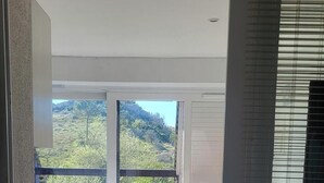 A room with a wooden floor, a bed, a table with chairs, and a large window offering a view of a hilly landscape. - Charming studio apartment, located in a quiet residential complex near the beach in Le Touquet (Paris)