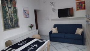 A living room with a blue sofa, a TV mounted on the wall, and a painting on the wall. - Vacation Apartments Along the Agropoli Seafront (Agropoli)