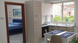 A compact kitchen with a dining area, a bed in the adjacent room, and a view of the outside. - Vacation Apartments Along the Agropoli Seafront (Agropoli)