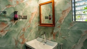 Ein Badezimmer mit Marmorwand, einem Waschbecken mit Wasserhahn, einem Spiegel und einem Fenster mit Jalousien.