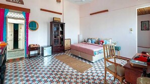 Ein Schlafzimmer mit gemustertem Boden, einem Bett, einem Schreibtisch, einem Kleiderschrank und einer mit Vorhängen versehenen Tür.
